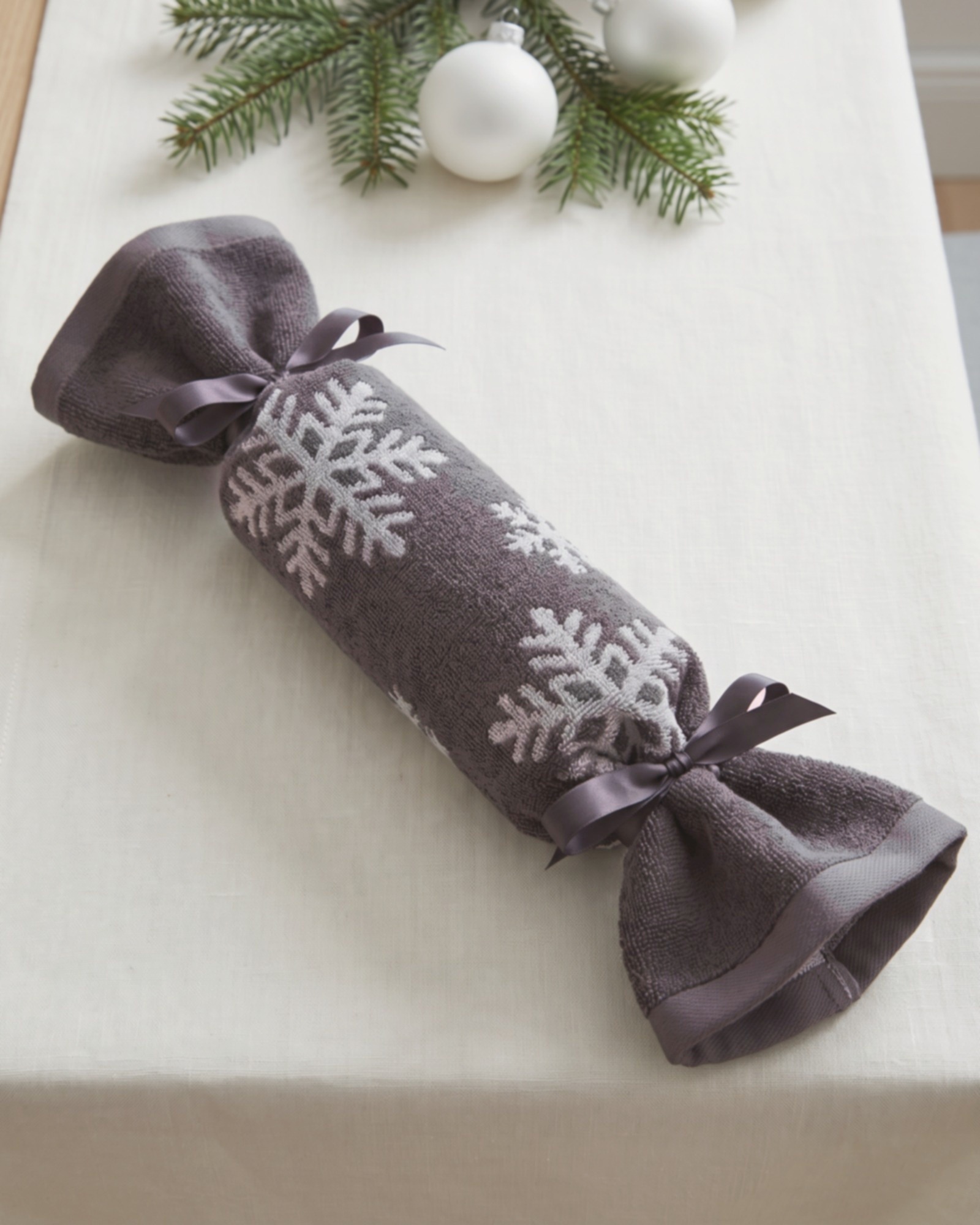 Christmas Cracker aus einem Handtuch in basalt/platin mit Schneekristallen, an beiden Enden mit Schleifenband gebunden