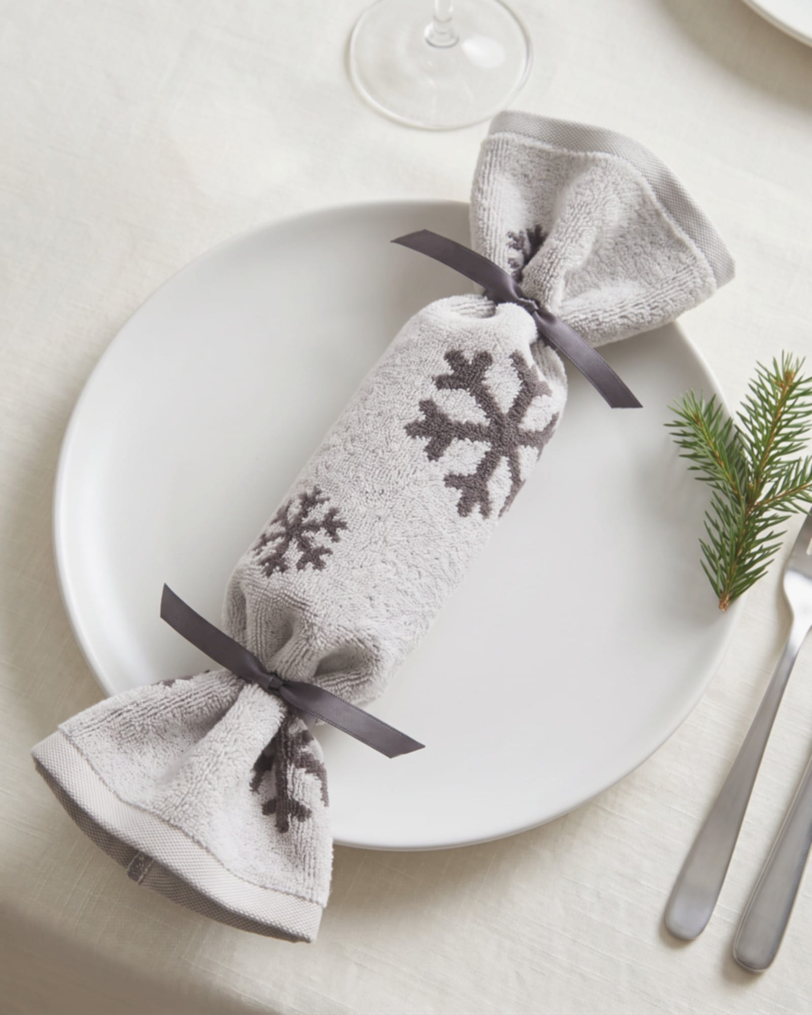 Christmas Cracker aus einem hellen Gästetuch mit dunklen Schneekristallen als Gästegeschenk auf einem Teller