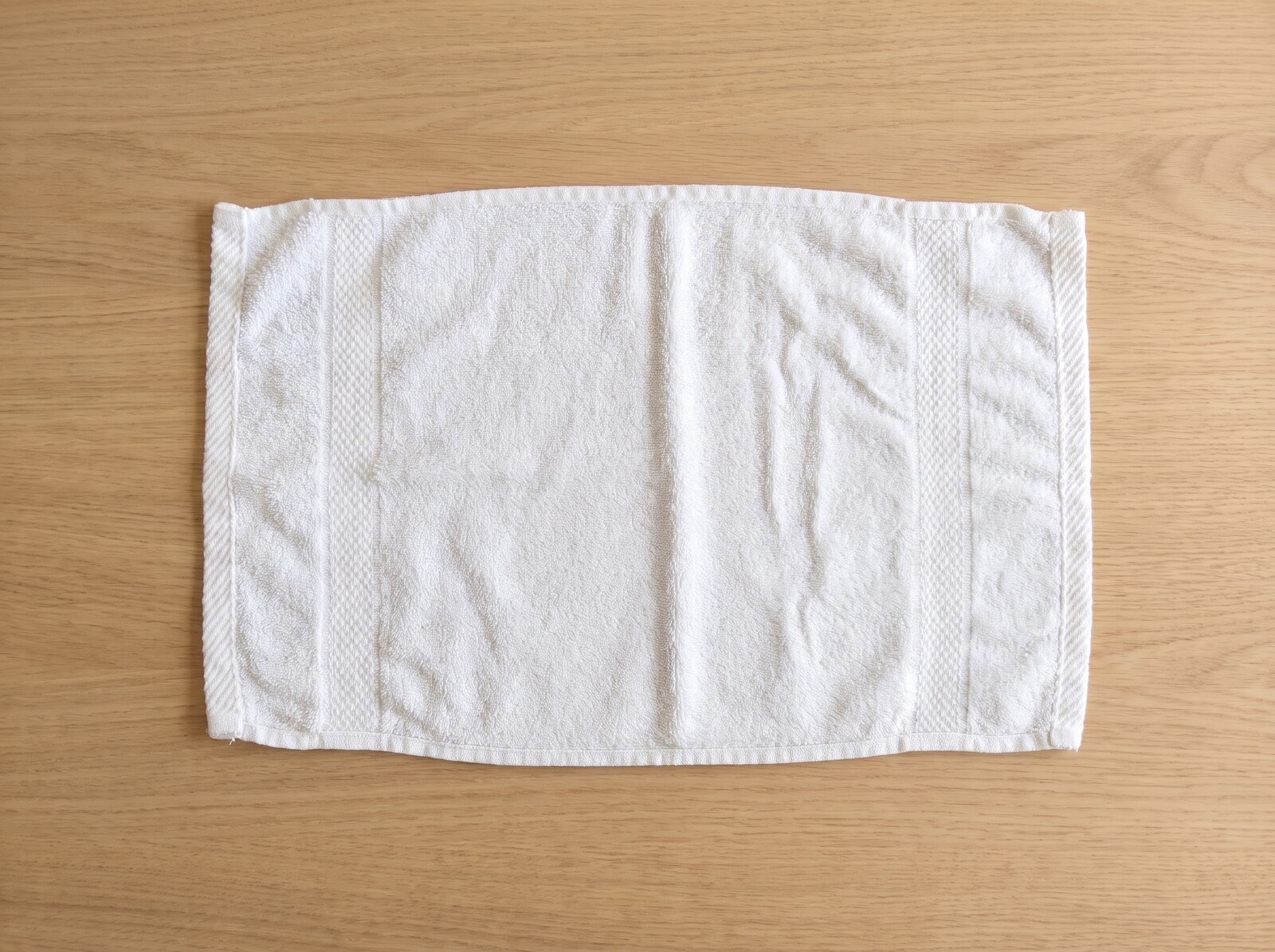 Schritt 1: weißes Gästetuch 30x50 cm liegt glatt gestrichen quer auf einem Holztisch