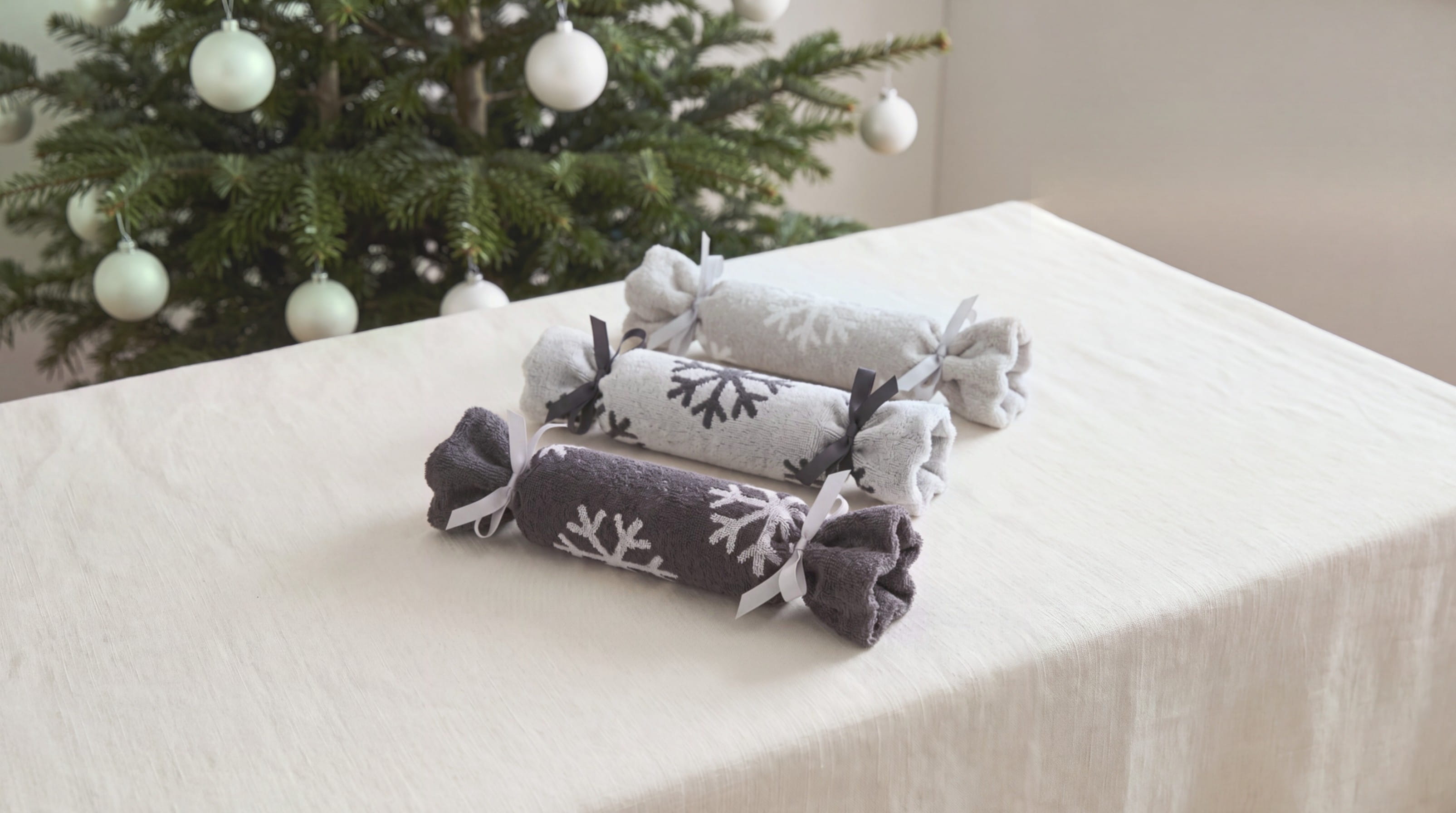 Drei Christmas Cracker aus Handtüchern der Cawö WINTER EDITION Schneekristalle auf einer festlich gedeckten Tafel vor dem Weihnachtsbaum